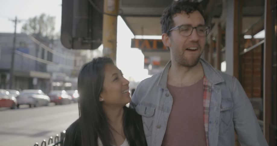 A man and woman walking down a city sidewalk and kissing