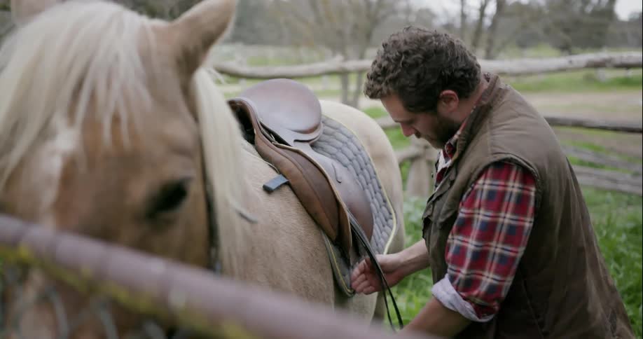 A man is putting a saddle on a horse