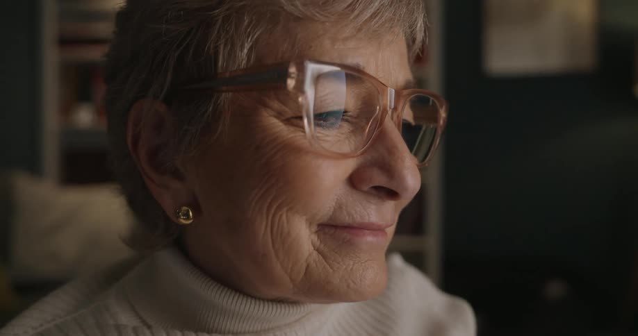 A happy elderly female is in a living room looking forward and smiling