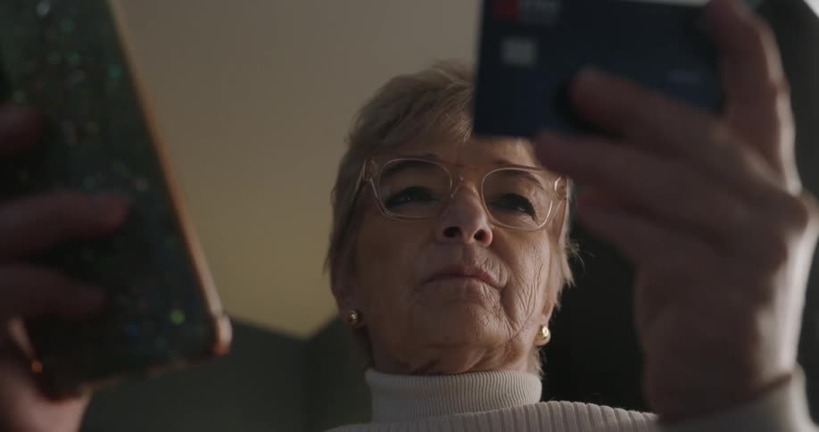Elderly woman holding a phone and a card in an indoor setting