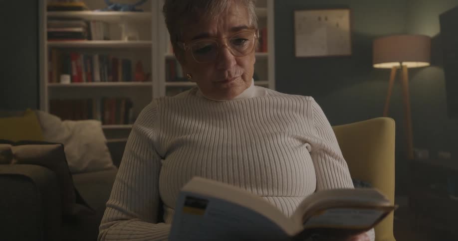 Elderly woman reading a book in a living room