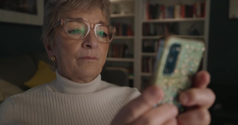 Adult woman wearing glasses and a white sweater holding a smartphone on her hand with a nervous facial expression indoors