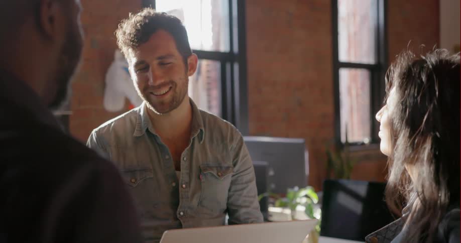 A man is using a laptop as he talks to others
