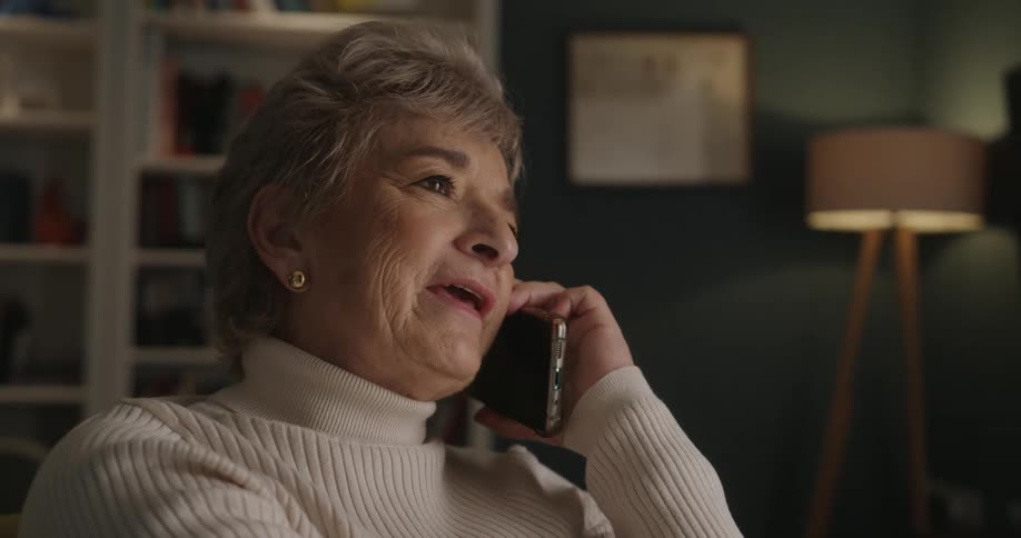 Woman smiles as she sits in her living room talking on the phone