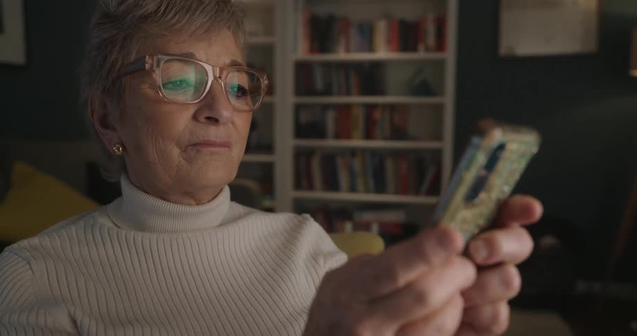 Woman puts on her glasses and starts texting on her phone as she sits in a living room chair