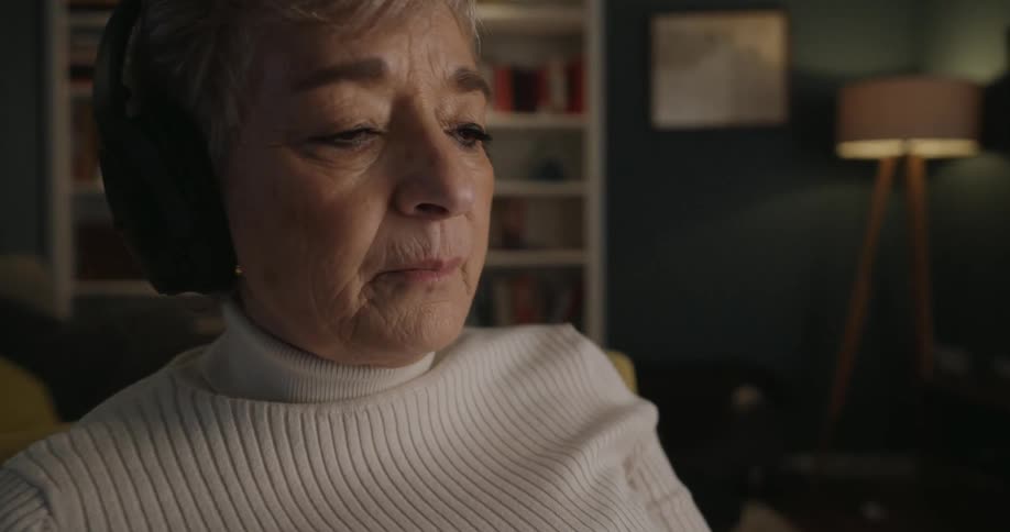 A woman is talking to her cellphone as she sits in a house