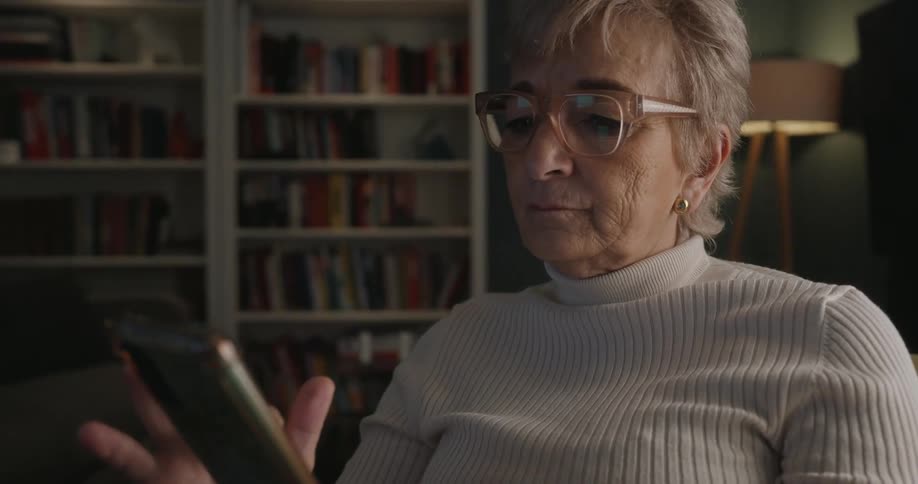 Woman looking at a smartphone while seated in a room with a bookshelf in the background