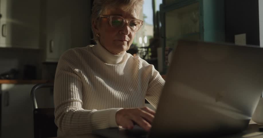 Woman sits at a table typing on a laptop computer