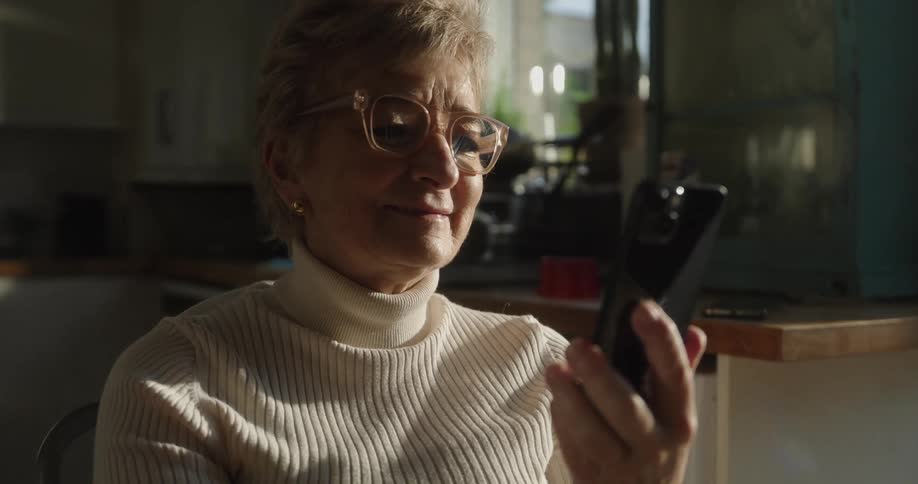 Woman holding a smartphone while looking at the screen in a lit kitchen