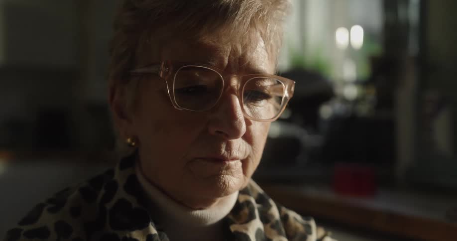 Elderly woman focuses while in her kitchen during the daytime
