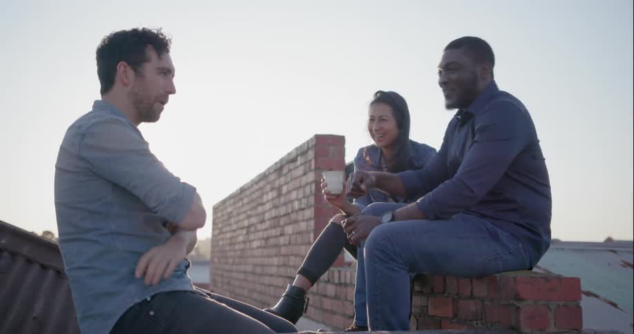 Three people talk while sitting on a rooftop