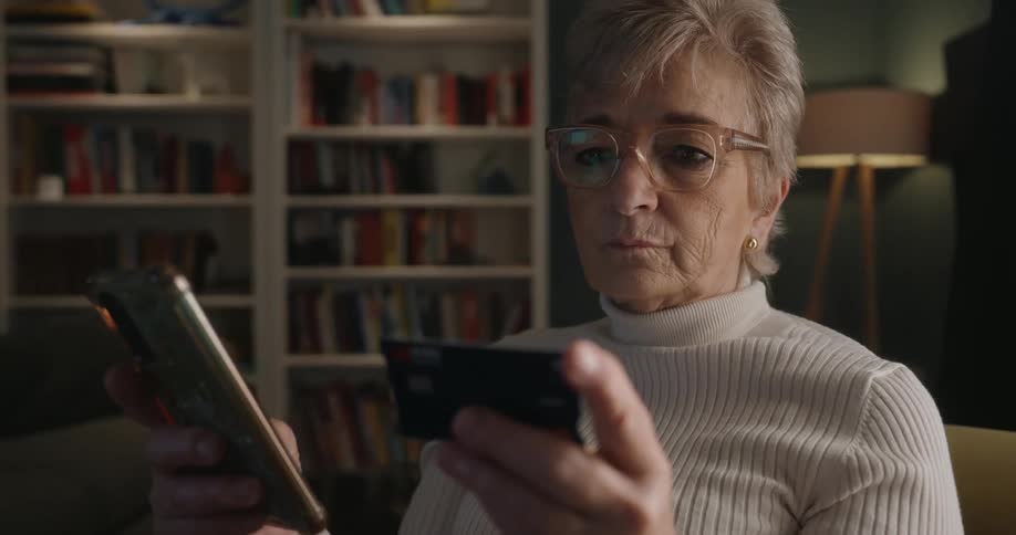 Elderly woman making an online transaction using a smartphone and credit card indoors