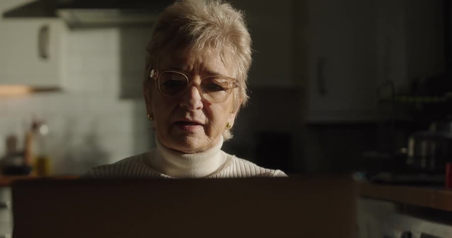 Woman wearing glasses looking at a laptop screen in a kitchen