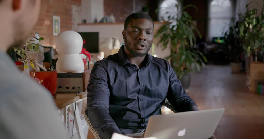 Man with a laptop on his lap talks to another man