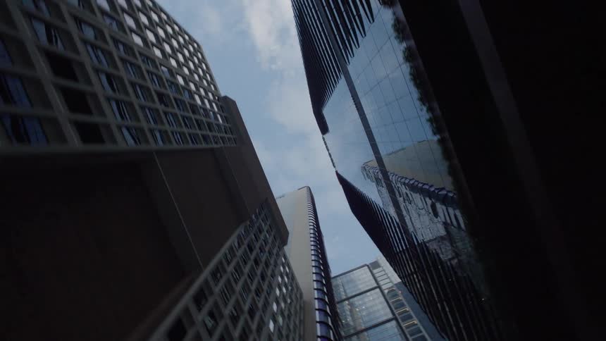 This is a dynamic lowangle shot looking up at several towering skyscrapers in a dense city environment with the buildings angling inwards toward the center of the frame the smooth glass and angular facades of the modern architecture contrast with the