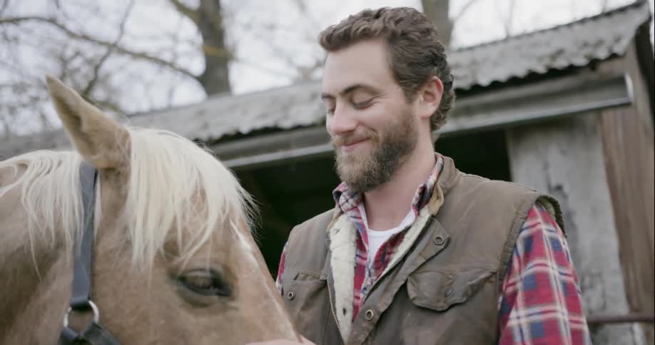 A man is petting his horse, and smiling