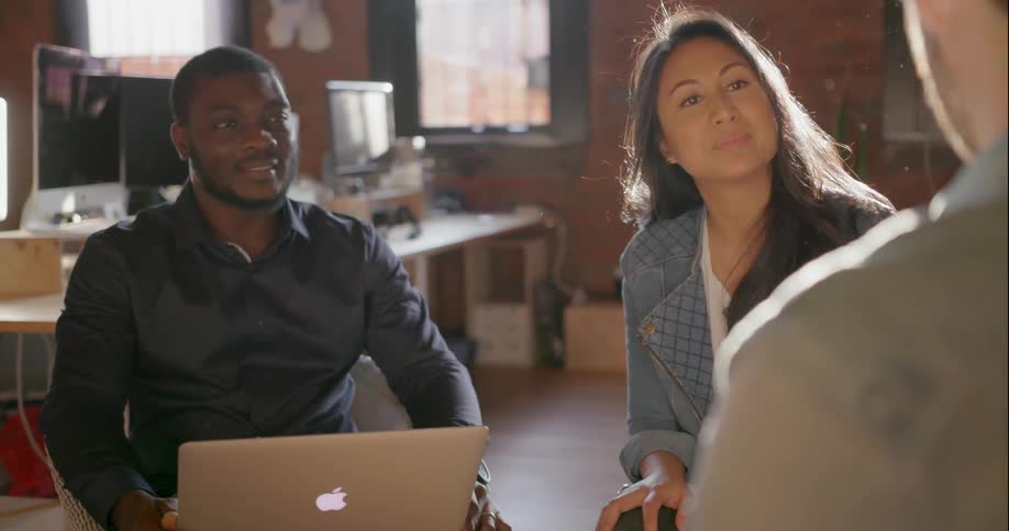 Two men and a woman sit and talk in an office on a sunny day