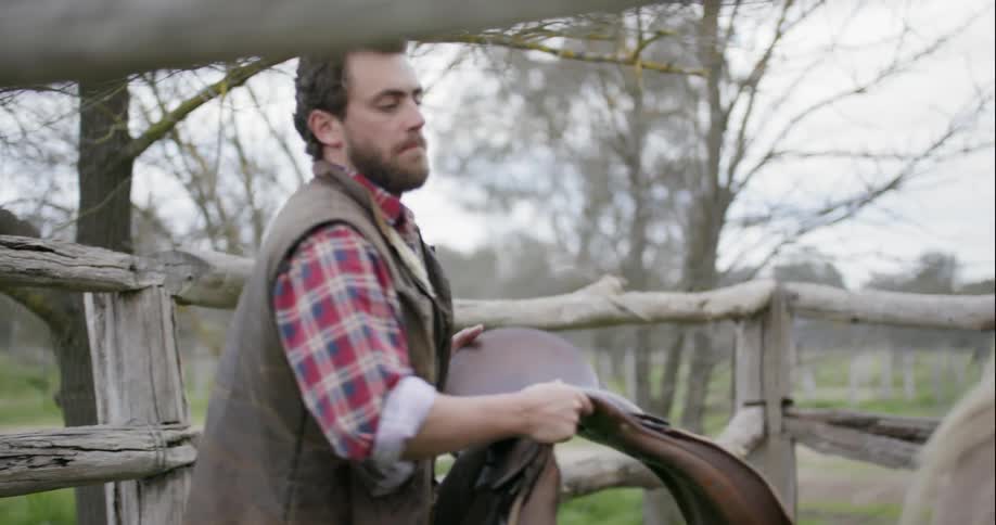 A man picks a saddle up and puts it on a horse