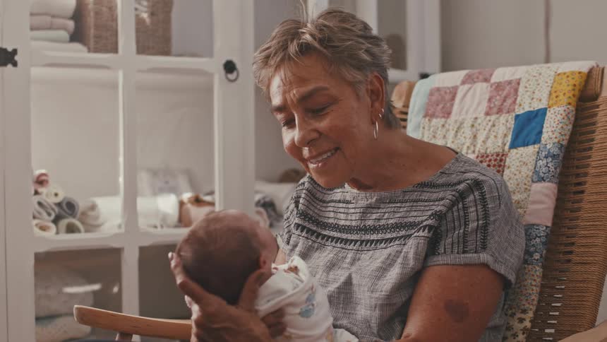 Woman seated holding a swaddled baby in a decorated room
