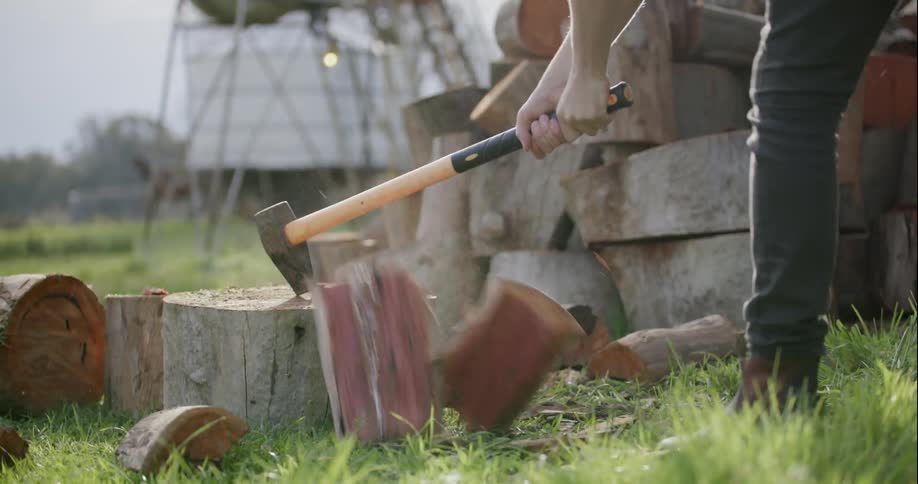 A man uses an ax to chop wood outside on a fall day