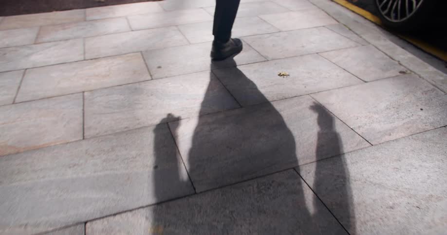 Legs of a person walking on the sidewalk towards a car in an urban area outdoors during day time