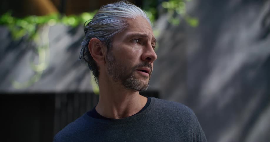 A middleaged man with distinctive gray and dark hair pulled back and a beard standing in an outdoor space