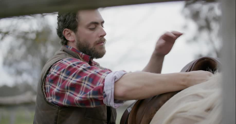 A man latches a saddle to a horse