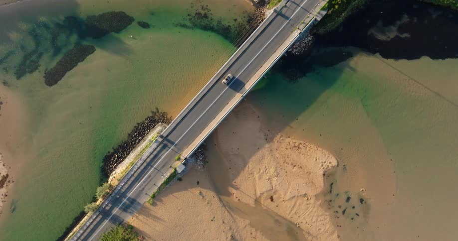 Aerial view of a concrete bridge and road spanning a shallow estuary beside sandy tidal flats