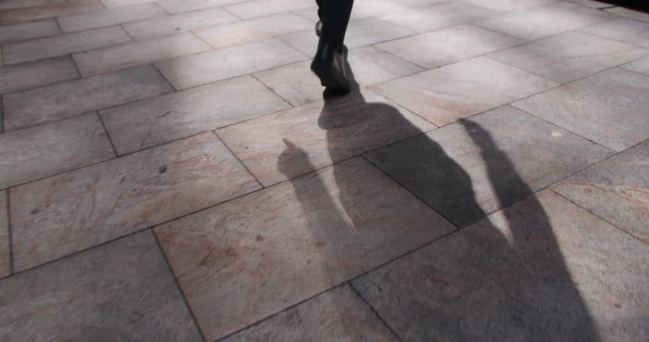 Legs of a person walking on light stone pavement