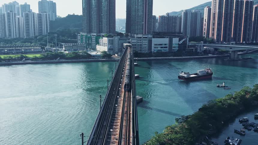 Train moving on a beam bridge leading over a body of water leading to a metropolitan area outdoors during day time