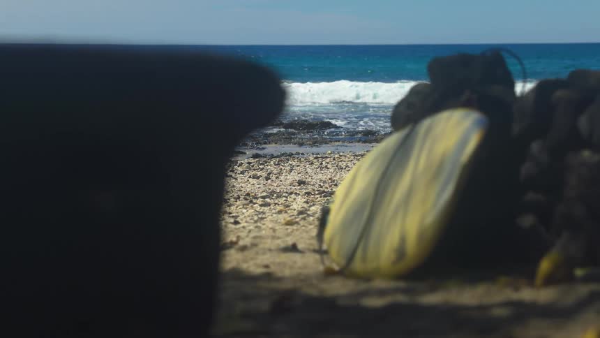 Surfboard lies on the beach near stacked rocks as the surf flows onto the beach during the day