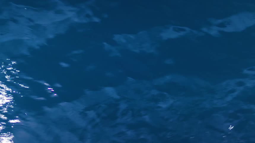 A dark blue body of water shows streaks of sunlight reflecting brightly off the surface in the distance