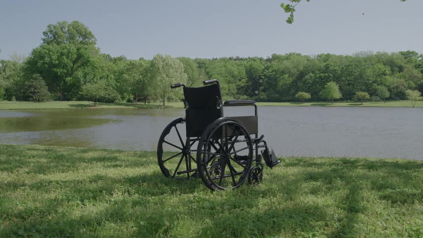 An empty wheelchair is on the grass next to a small lake