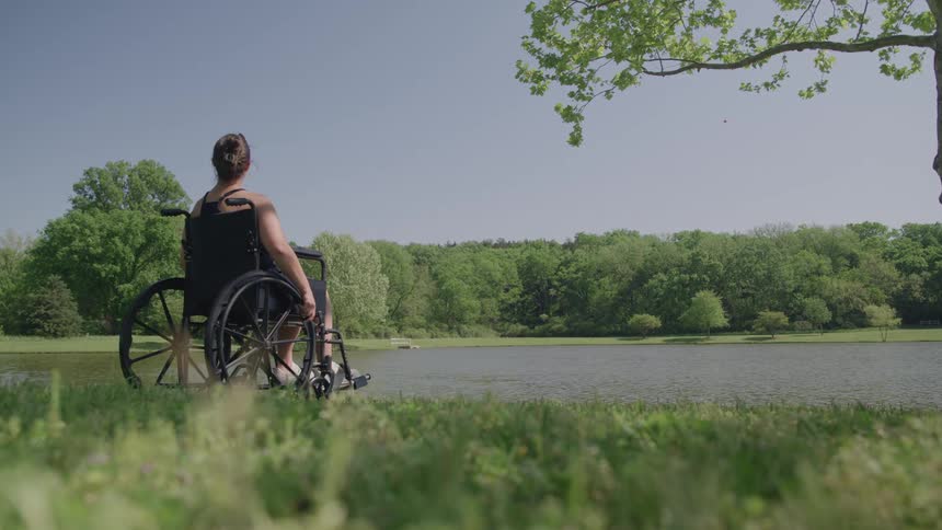 Woman in a wheelchair by a lake in a wooded area