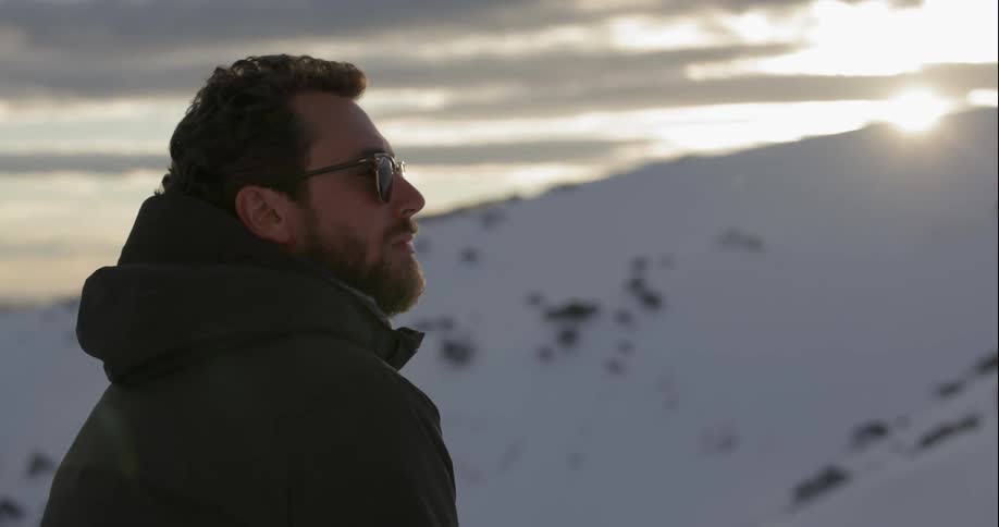 Man looks out at snowy terrain on a sunny day