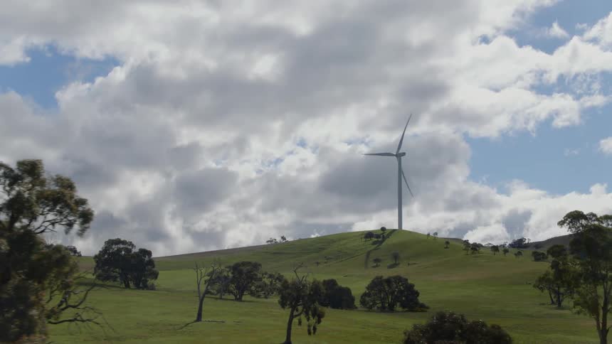 A wind turbine spins atop a hill on a cloudy day
