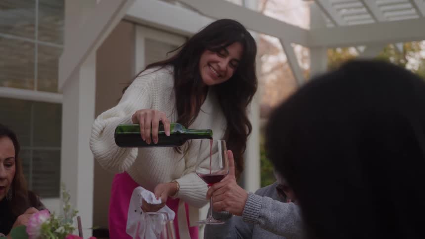 A waitress is pouring a glass of wine for a man sitting at a table in a restaurant with two women
