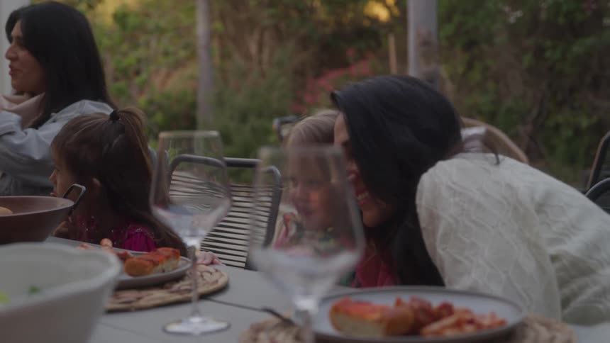 Mother leans against her child while an extended family eats outdoors near a steep slope
