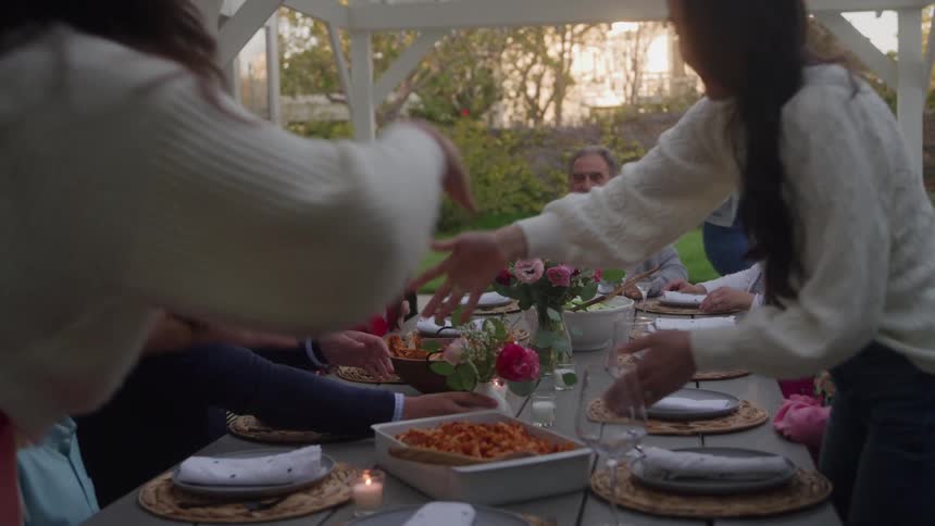 A family gathers around an outdoor table to share a meal in the evening