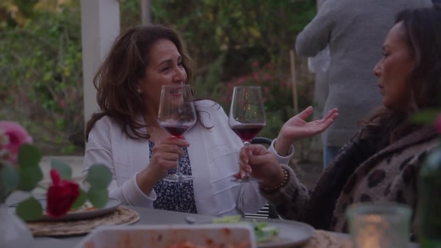 Women are sitting at an outdoor table at a restaurant drinking wine and talking