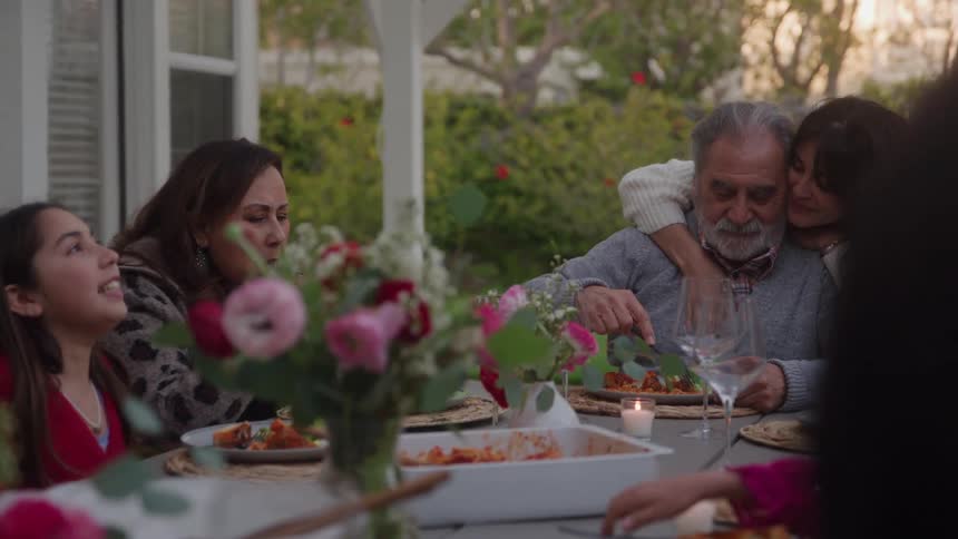 A family is gathered at a table in their backyard and share a meal together