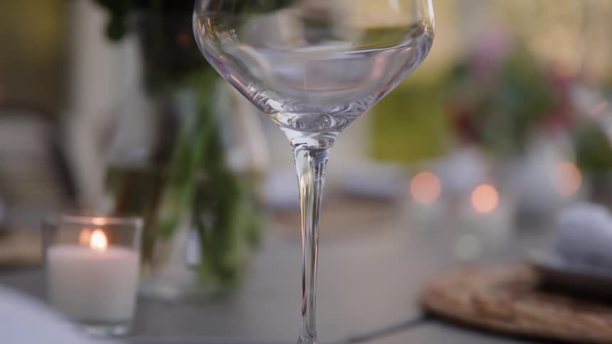 Lit candles on a table as red wine fills an empty glass
