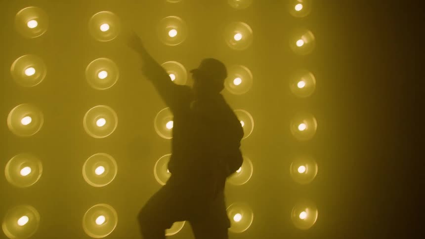 Silhouette of a person dancing in front of a wall illuminated by circular blue and green lights