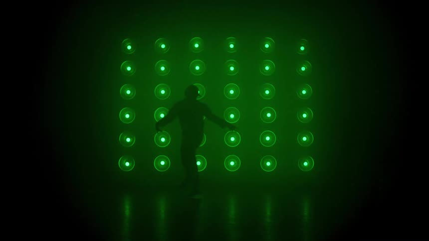 A male dancer dancing is silhouetted against a large grid of white and magenta stage lights in a dark foggy studio