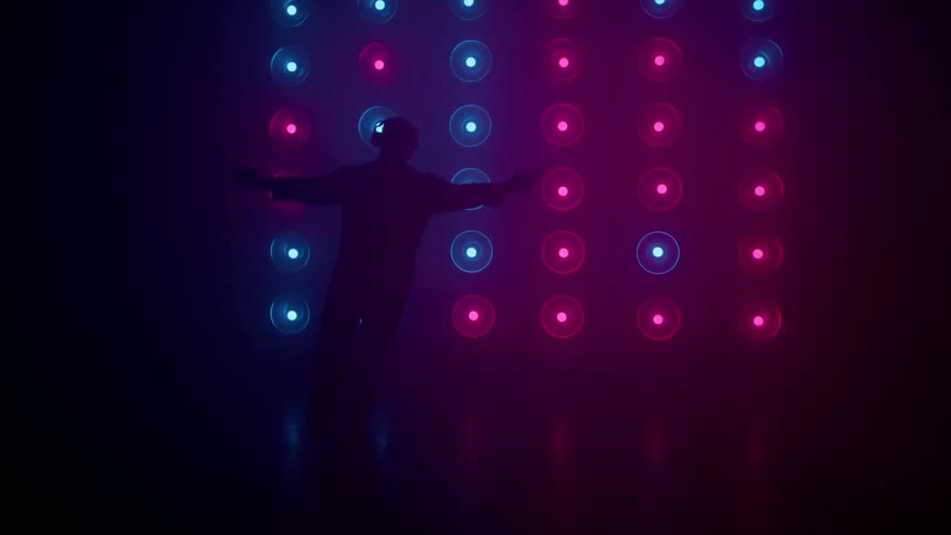 Silhouette of a young man dancing on a disco stage while listening to music with headphones
