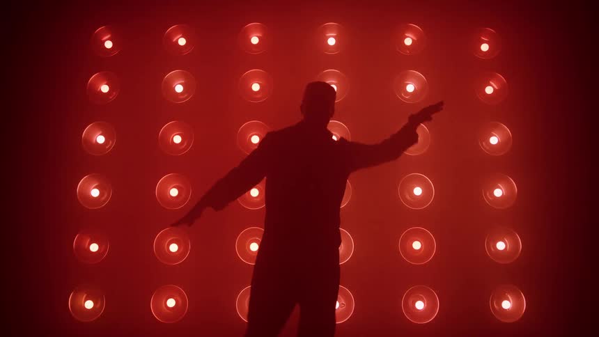 The video features a dancer in silhouette against a large grid of lights that rapidly change color creating a vibrant highenergy backdropthe silhouette performs a synchronized dance with their arms stretched out while the lights transition between