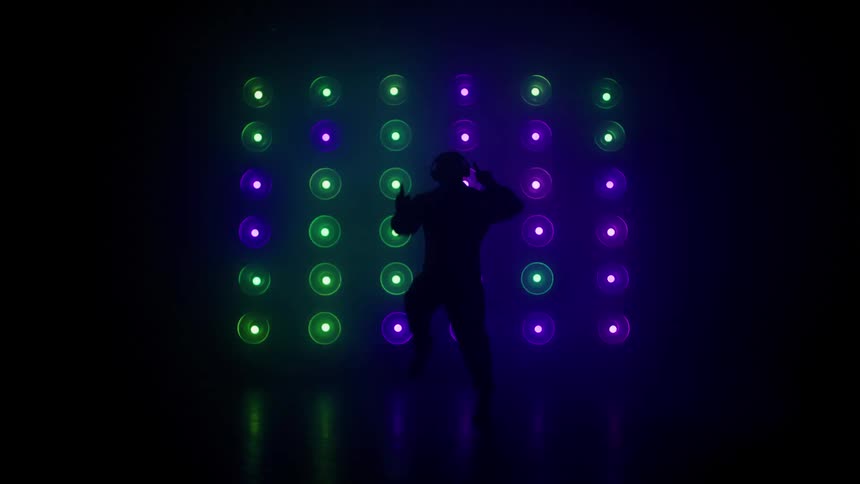A male dancer performs in front of a wall of colorful flashing light bulbs