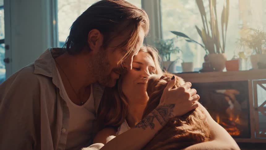 A man and woman are close together as they hug and pet a dog in the womans arms