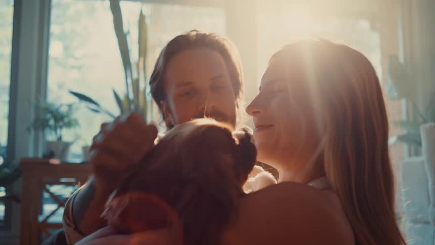 A happy man and woman lovingly hug their brown dog in a sundrenched living room