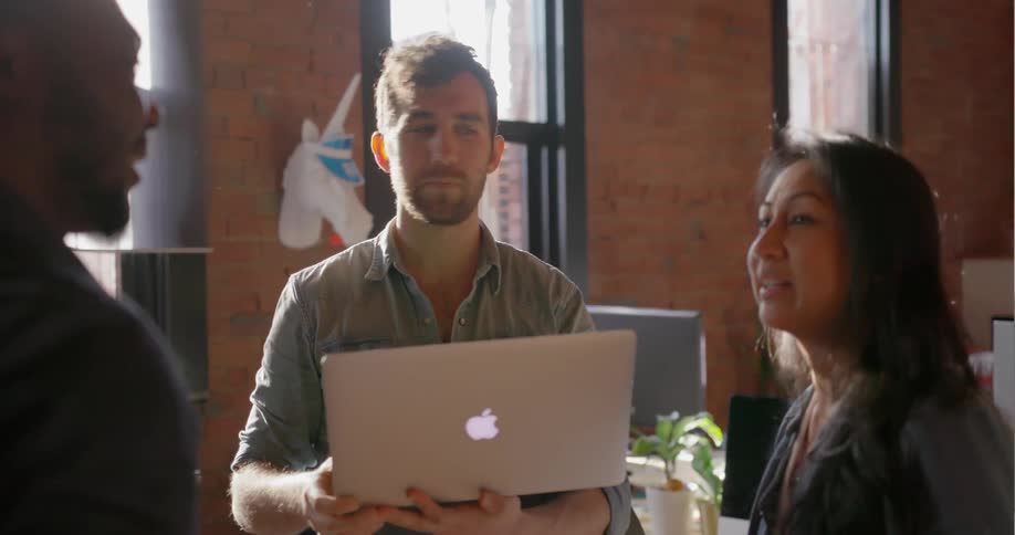 People stand together in an office talking and using a laptop